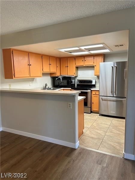 kitchen featuring light wood-type flooring, kitchen peninsula, appliances with stainless steel finishes, and a textured ceiling