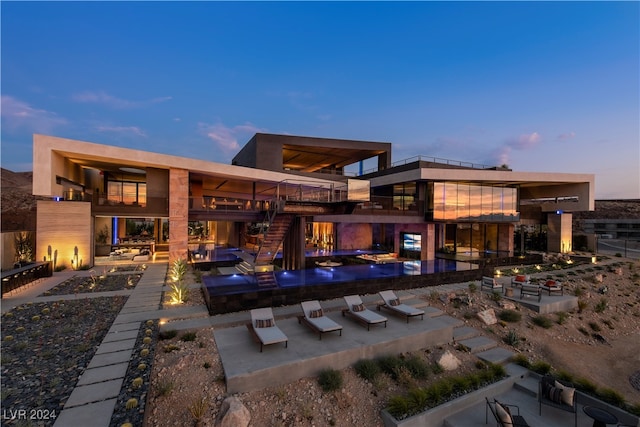 back house at dusk featuring a patio area and a balcony