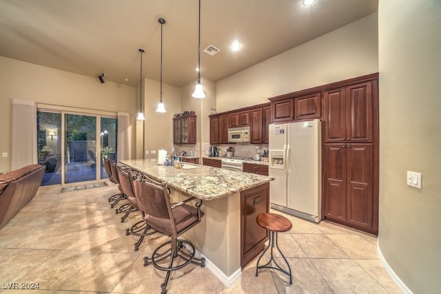 kitchen with hanging light fixtures, white appliances, a center island with sink, a kitchen breakfast bar, and light stone countertops