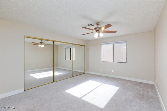 unfurnished bedroom featuring ceiling fan, a textured ceiling, a closet, and light carpet