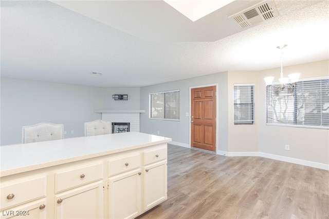 kitchen with light hardwood / wood-style floors, a textured ceiling, a notable chandelier, hanging light fixtures, and a fireplace