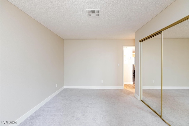 unfurnished bedroom with a textured ceiling, carpet flooring, and a closet