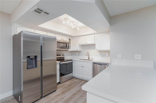 kitchen with a raised ceiling, sink, white cabinetry, stainless steel appliances, and light hardwood / wood-style floors