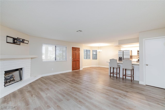 living room with light wood-type flooring, a textured ceiling, a fireplace, and an inviting chandelier