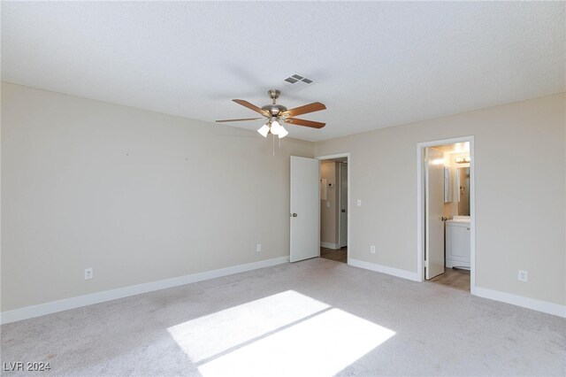 unfurnished bedroom with ceiling fan, a textured ceiling, light carpet, and ensuite bathroom