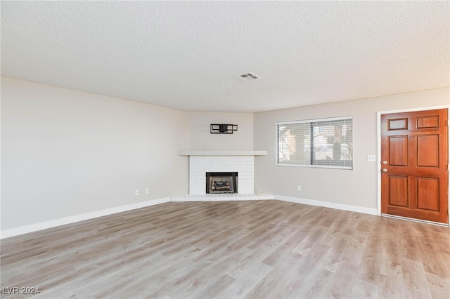 unfurnished living room featuring a brick fireplace, light hardwood / wood-style floors, and a textured ceiling