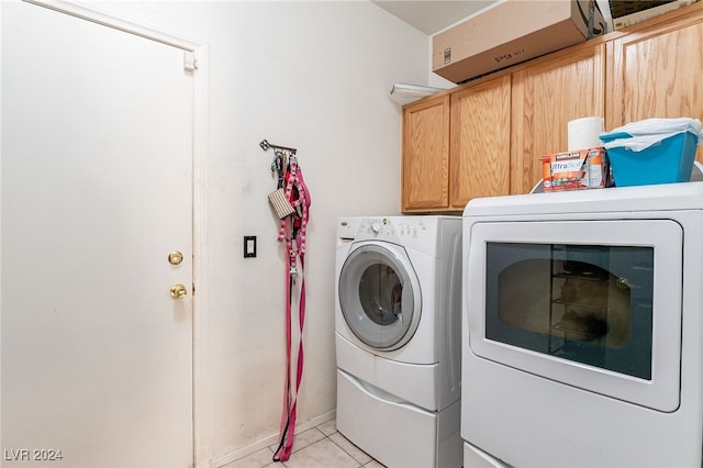 clothes washing area featuring washer and dryer, light tile patterned flooring, and cabinets