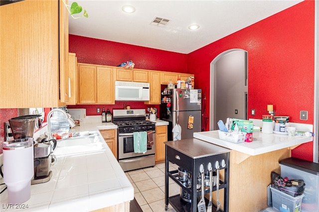 kitchen with tile counters, light tile patterned floors, sink, and appliances with stainless steel finishes