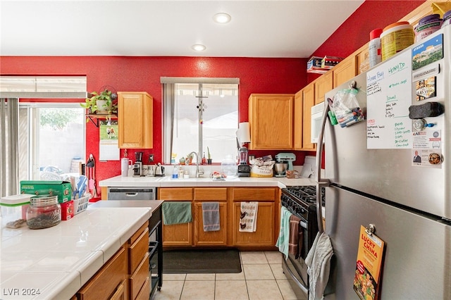 kitchen featuring tile countertops, light tile patterned flooring, sink, and appliances with stainless steel finishes