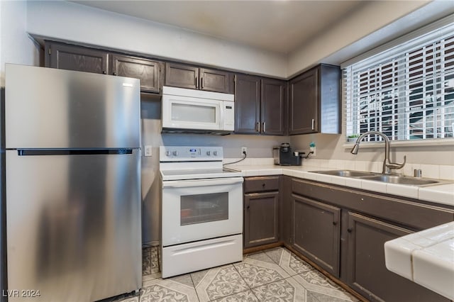 kitchen featuring dark brown cabinetry, light tile patterned floors, sink, white appliances, and tile countertops