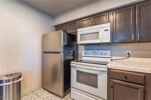 kitchen featuring dark brown cabinetry, light tile patterned floors, tile counters, and white appliances