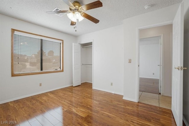 unfurnished bedroom featuring a textured ceiling, a closet, hardwood / wood-style floors, and ceiling fan