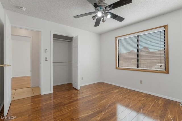 unfurnished bedroom with ceiling fan, a textured ceiling, a closet, and hardwood / wood-style floors