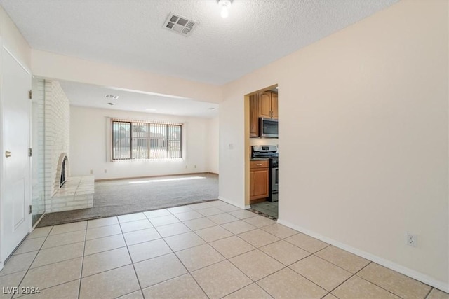 spare room featuring a fireplace, a textured ceiling, and light tile patterned flooring