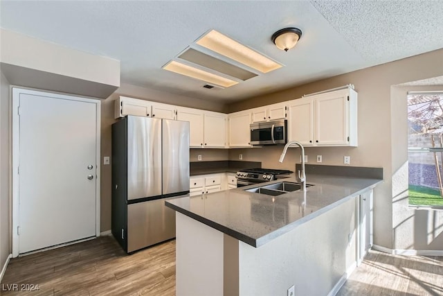 kitchen with wood-type flooring, kitchen peninsula, sink, white cabinetry, and stainless steel appliances