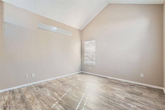 spare room with lofted ceiling, a textured ceiling, and light hardwood / wood-style flooring