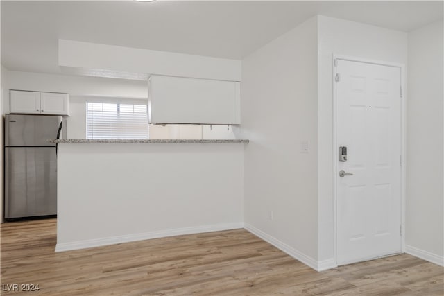 kitchen featuring light stone counters, white cabinetry, kitchen peninsula, stainless steel refrigerator, and light hardwood / wood-style flooring