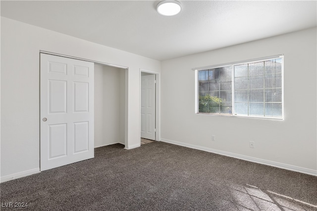 unfurnished bedroom with dark carpet and a closet