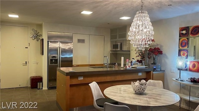 kitchen with dark tile patterned flooring, sink, kitchen peninsula, stainless steel appliances, and an inviting chandelier