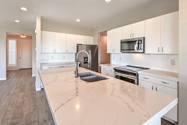 kitchen featuring wood-type flooring, white cabinets, stainless steel appliances, and light stone countertops