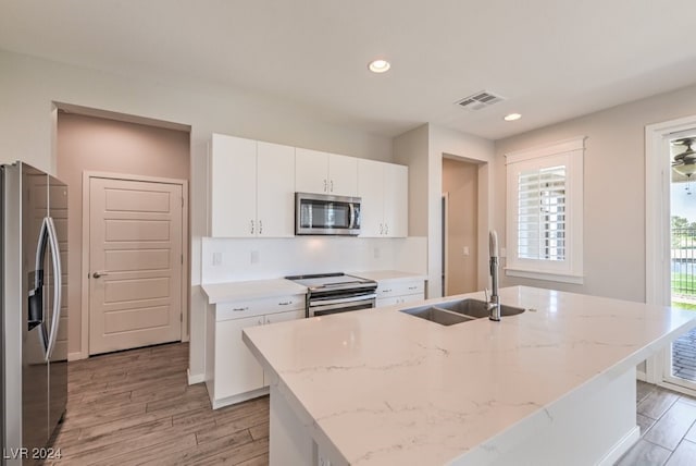 kitchen with appliances with stainless steel finishes, light hardwood / wood-style floors, sink, and an island with sink