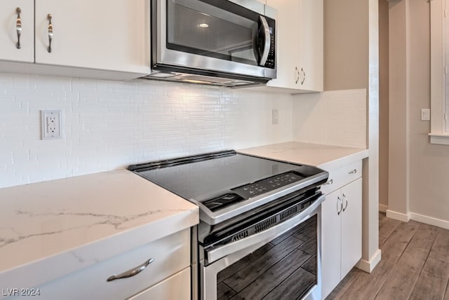 kitchen with white cabinets, tasteful backsplash, light hardwood / wood-style flooring, stainless steel appliances, and light stone countertops