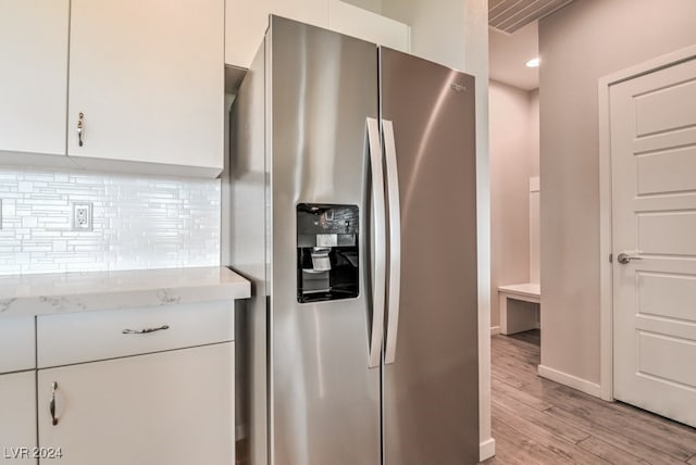 kitchen featuring white cabinets, stainless steel refrigerator with ice dispenser, light hardwood / wood-style flooring, and decorative backsplash