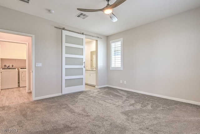 unfurnished bedroom with ceiling fan, washing machine and clothes dryer, a barn door, light colored carpet, and ensuite bathroom