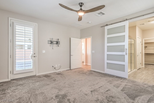 unfurnished bedroom with a barn door, a spacious closet, ceiling fan, and light colored carpet