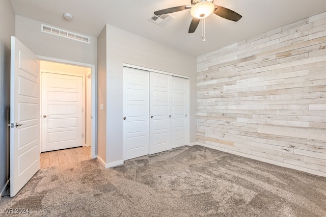 unfurnished bedroom with ceiling fan, light colored carpet, wooden walls, and a closet