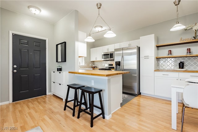 kitchen featuring appliances with stainless steel finishes, decorative light fixtures, butcher block countertops, and white cabinetry