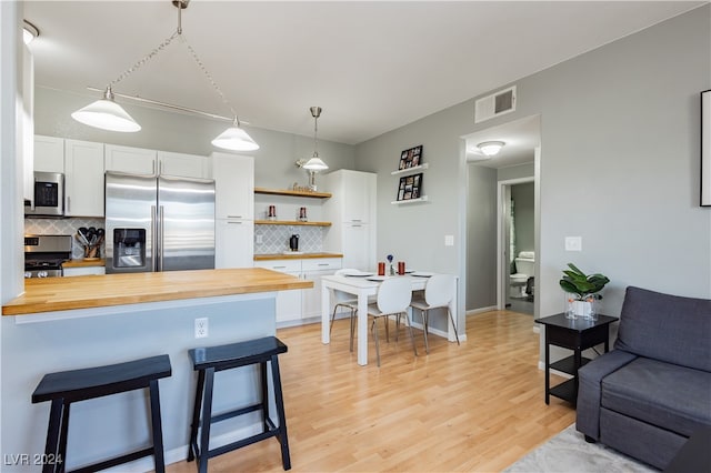 kitchen featuring butcher block countertops, stainless steel appliances, a kitchen breakfast bar, and white cabinetry