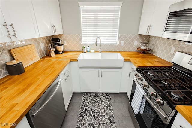 kitchen featuring dark tile patterned floors, sink, white cabinets, appliances with stainless steel finishes, and butcher block countertops