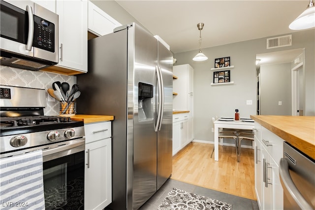 kitchen featuring light wood-type flooring, wood counters, white cabinetry, appliances with stainless steel finishes, and decorative light fixtures