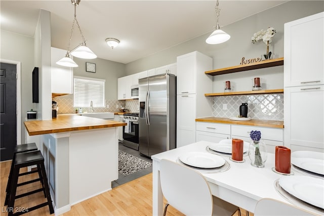 kitchen with hanging light fixtures, wood counters, stainless steel appliances, and white cabinets