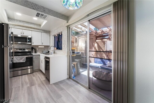 kitchen with white cabinetry, a raised ceiling, stainless steel appliances, light wood-type flooring, and sink