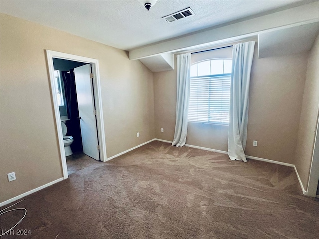 unfurnished bedroom with a textured ceiling, carpet, and ensuite bath