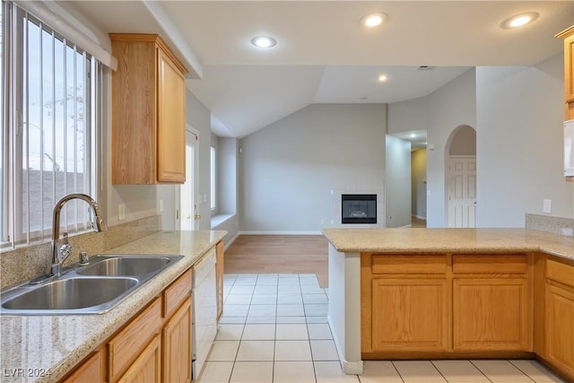 kitchen featuring lofted ceiling, white dishwasher, sink, light tile patterned floors, and a fireplace