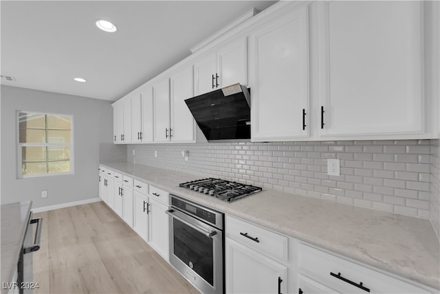 kitchen with light stone counters, light hardwood / wood-style flooring, white cabinetry, appliances with stainless steel finishes, and decorative backsplash