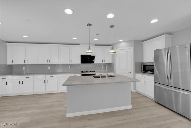 kitchen featuring pendant lighting, an island with sink, sink, stainless steel appliances, and light wood-type flooring