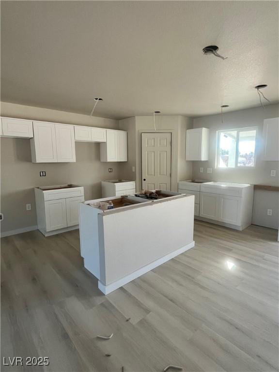 kitchen with light wood-style floors, white cabinets, a kitchen island, and baseboards