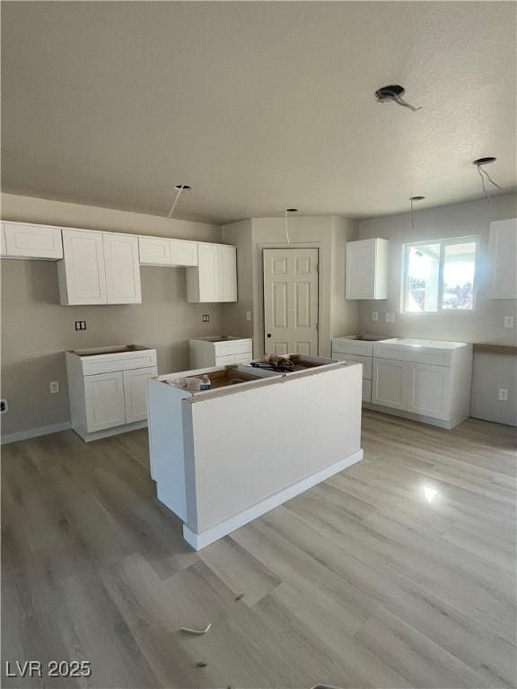 kitchen with light wood-style flooring, white cabinets, a textured ceiling, and a center island