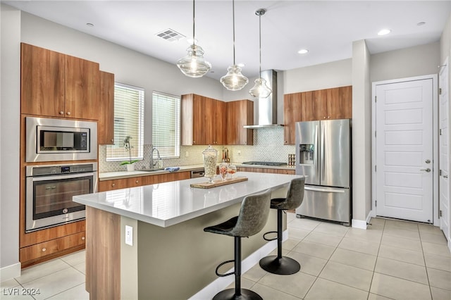 kitchen with a breakfast bar, appliances with stainless steel finishes, hanging light fixtures, a kitchen island, and wall chimney range hood