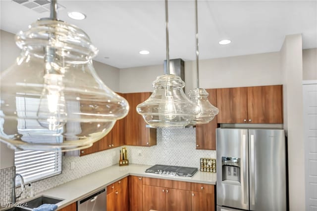 kitchen with stainless steel appliances, sink, island range hood, backsplash, and hanging light fixtures