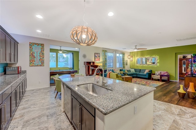 kitchen with sink, light stone counters, light hardwood / wood-style flooring, dark brown cabinets, and a center island with sink