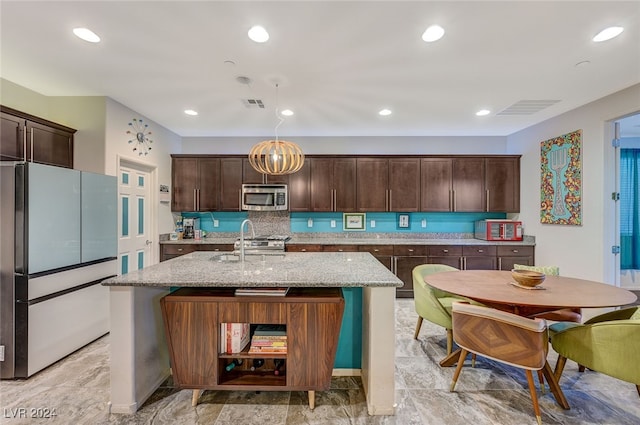 kitchen with a center island with sink, decorative light fixtures, dark brown cabinets, light stone counters, and stainless steel appliances