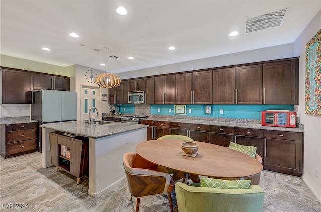 kitchen featuring sink, pendant lighting, a kitchen island with sink, dark brown cabinets, and appliances with stainless steel finishes