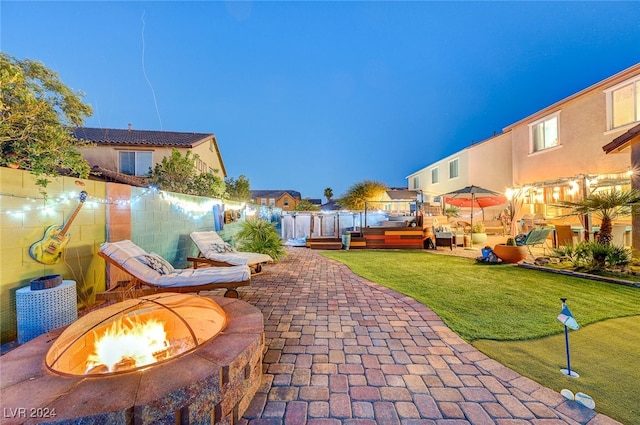 patio terrace at dusk featuring a fire pit, a deck, and a yard