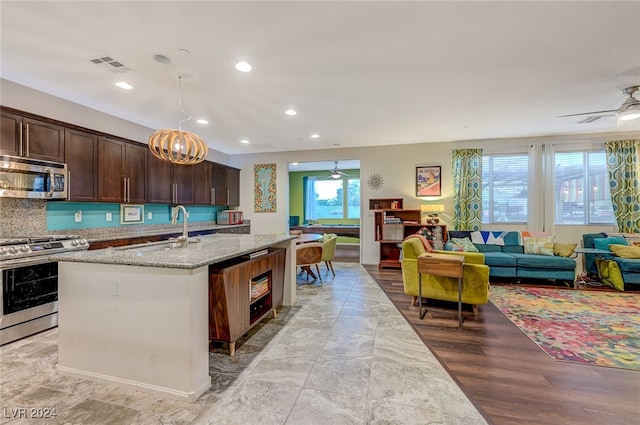 kitchen with dark brown cabinetry, light stone countertops, sink, stainless steel appliances, and an island with sink