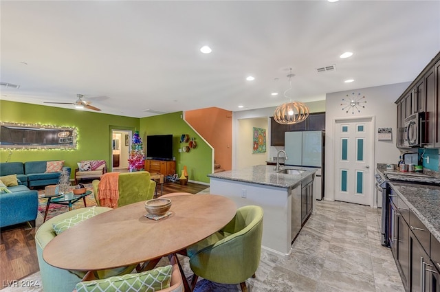 kitchen with light stone countertops, pendant lighting, a kitchen island with sink, dark brown cabinets, and appliances with stainless steel finishes